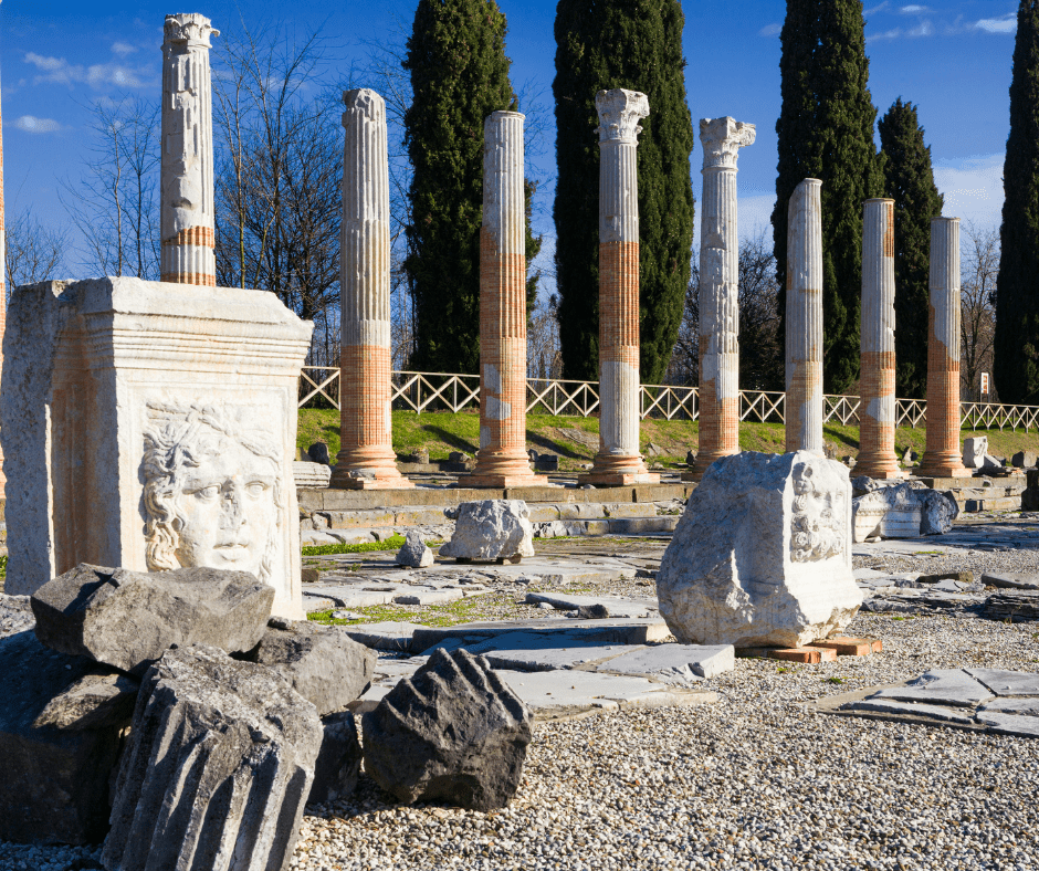 Ancient ruins in Aquileia, Italy, featuring Roman columns, mosaic floors, and the Basilica of Aquileia in the background—once a major Roman port and cultural hub.
