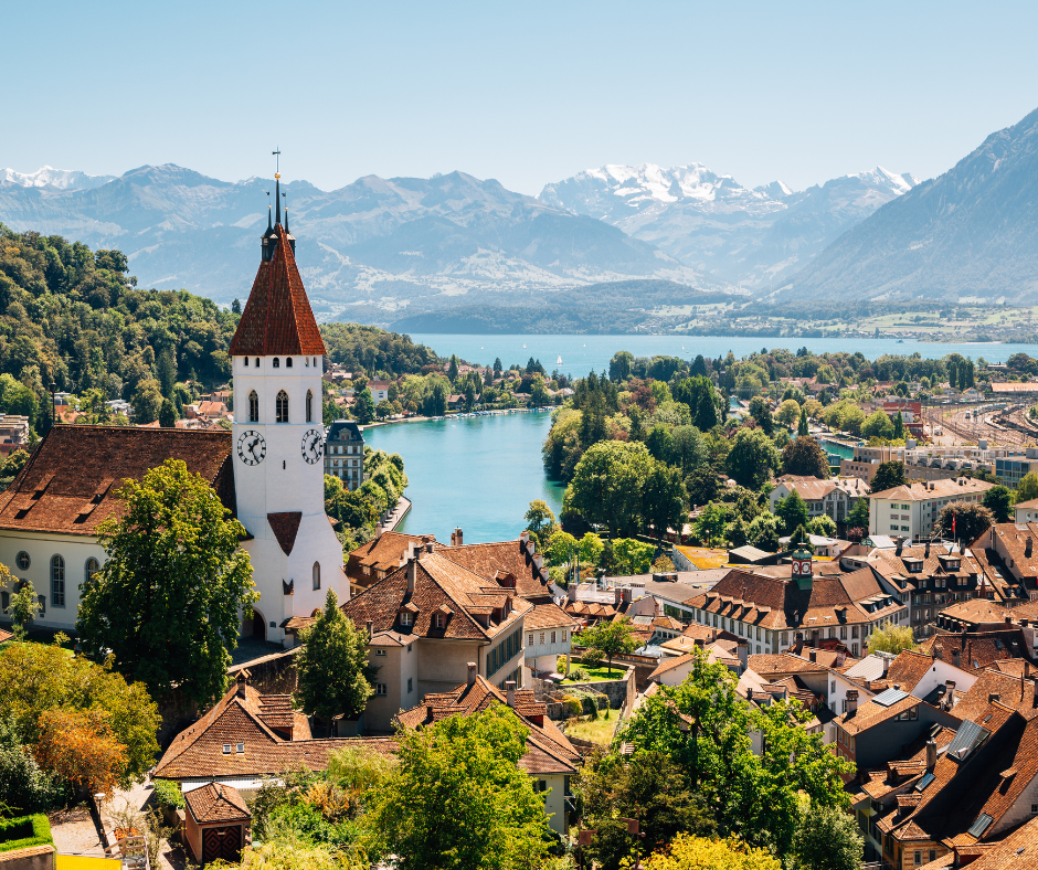 Panoramic view of Thun cityscape with the beautiful Swiss Alps in the background, and Lake Thun's crystal-clear waters stretching across the foreground, capturing the serene beauty of this picturesque Swiss town. 