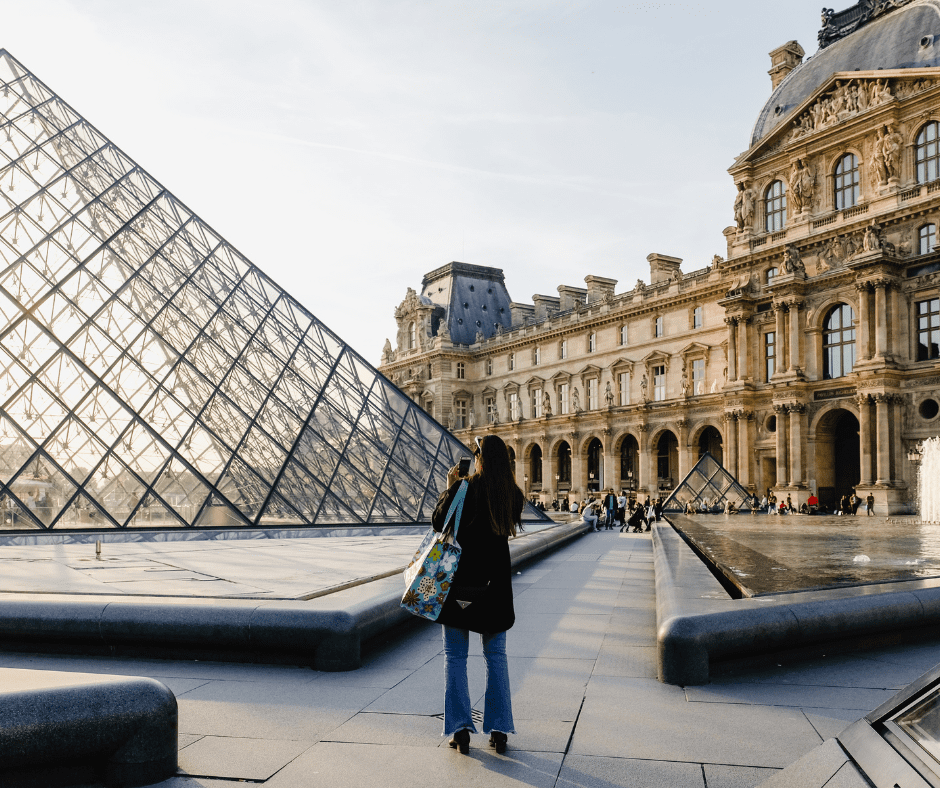 Woman photographing the Louvre Museum at golden hour, capturing the scene in soft natural light.